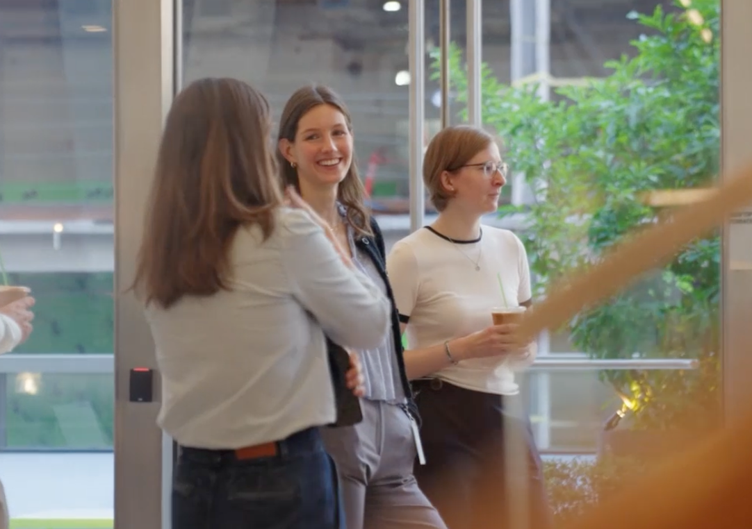 Three colleagues talking together in a bright modern office with greenery outside the windows